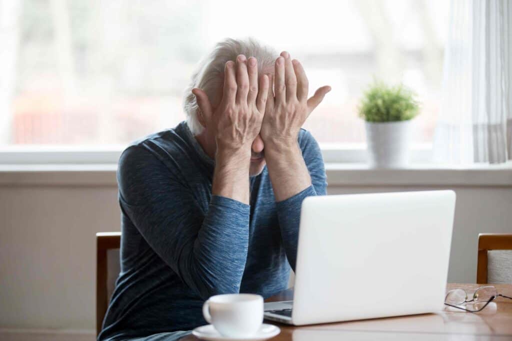 Fatigued senior man sitting in front of a laptop rubs his eyes-compressed